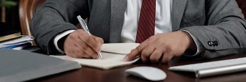 Businessman sitting at a wood desk writing on a pad of paper